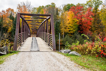 Empty Steel Pedestrian And Bicycle Bridge Spanning A River With Forested Banks At The Peak Of Fall Foliage