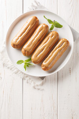 Wall Mural - Fresh classic eclairs with cream filling and covered with caramel sauce close-up in a plate on the table. Vertical top view from above