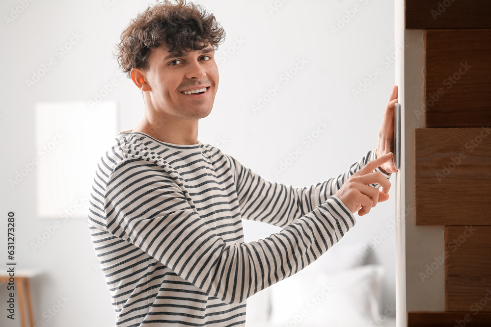 Young man using smart home security system control panel in bedroom
