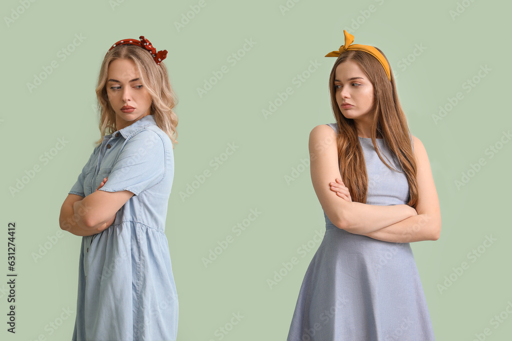 Upset young sisters on green background