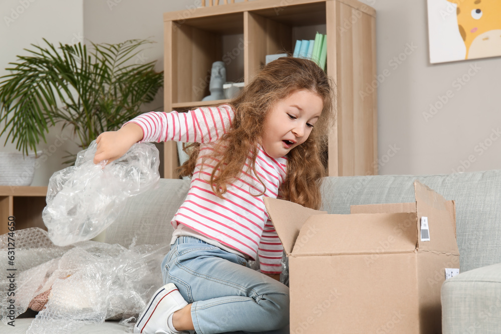 Surprised little girl unpacking parcel at home