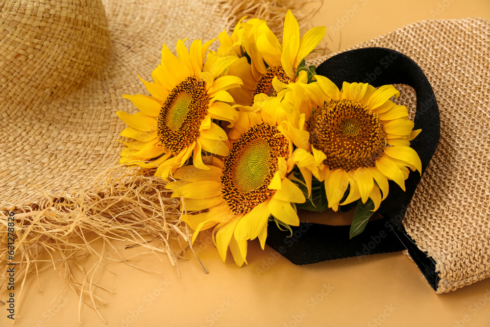 Stylish straw bag with hat and beautiful sunflowers on orange background