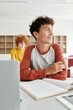 © LIGHTFIELD STUDIOS - Smiling teenage schoolboy holding pencil near notebook and devices during lesson in school