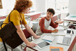 © LIGHTFIELD STUDIOS - Teenage schoolboy talking to friend with backpack near devices and notebooks on desk in classroom