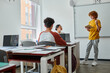 © LIGHTFIELD STUDIOS - Redhead teen schoolboy holding book and talking near african american teacher during lesson in class