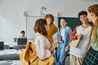 © LIGHTFIELD STUDIOS - Cheerful teenage pupils with notebook and smartphone standing near blurred friend in classroom