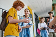 © LIGHTFIELD STUDIOS - back to school, classmates using gadgets in school hallway, redhead boy using smartphone near girl