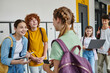 © LIGHTFIELD STUDIOS - back to school, teenagers talking in school hallway, holding devices and chatting with each other