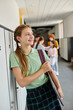 © LIGHTFIELD STUDIOS - cheerful teenage girl holding laptop and looking away in hallway, back to school concept, modern age