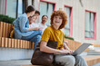 © LIGHTFIELD STUDIOS - back to school, happy redhead boy with curly hair using laptop near classmates and teacher, blur
