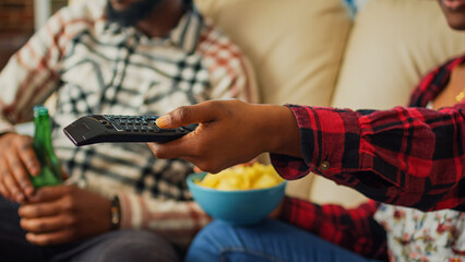 Wall Mural - Girlfriend switching channels on television to find movie, using tv remote control to watch favorite film or show with man. Young couple eating chips and drinking beer at home. Close up.