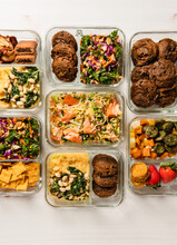 Meal Prep Containers With Salad, Salmon, Fruit, Polenta, Cookies, Sausage, Vegetables, Potatoes And Snacks