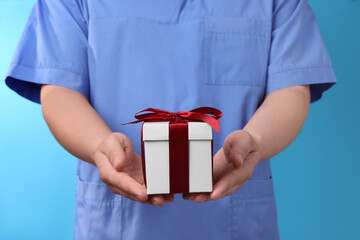 Doctor holding gift box on light blue background, closeup. Medical present