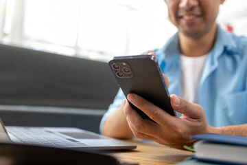 Asian man holding cell phone, he is texting via smartphone application talking to friends, using smartphone to send text messages over the internet. The concept of using technology in communication.