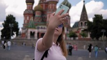 A Happy Tourist Takes A Selfie Standing On Red Square Against The Background Of A Church. A Woman With A Phone Walks Around The City And Takes Pictures. St. Basil's Cathedral.