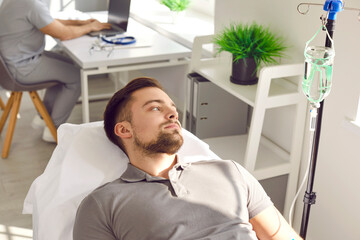 Male patient receives intravenous medical infusion at clinic or hospital. Young man lying on bed and getting medication or vitamin solution through sterile IV line. Medicine, therapy treatment concept