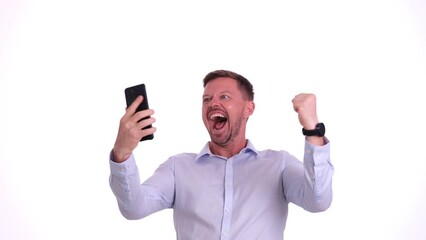 Young bearded man takes out mobile phone from pocket and exclaims happily looking at screen. Guy shouts and waves fists joyfully receiving win notification