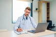 © kelvn - Male Doctor expert wearing white coat using laptop and reading clipboard report at work in hospital.
