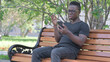 © stockbakers - Young African Man Shocked by Loss on Smartphone while Sitting Outdoor on a Bench