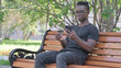 © stockbakers - Young African Man Doing Online Shopping on phone while Sitting Outdoor on a Bench