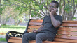 © stockbakers - Young African Man Talking on phone while Sitting Outdoor on a Bench
