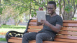 © stockbakers - Young African Man Celebrating Success on Tablet while Sitting Outdoor on a Bench