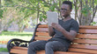© stockbakers - Young African Man Upset by Loss on Tablet while Sitting Outdoor on a Bench