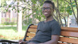 © stockbakers - Smiling Young African Man Sitting Outdoor and Looking at Camera