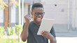 © stockbakers - Young African Man Celebrating Success on Tablet Outdoor