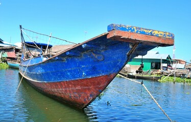 Sticker - Old blue boat is pictured in the foreground on calm waters, with a dock in the background