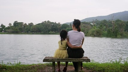 Wall Mural - Little girl sitting on the park bench and hugging her mother at dusk.