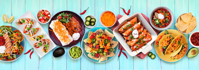 Wall Mural - Mexican food table scene. Top down view on a blue wood banner background. Tacos, burrito plate, nachos, enchiladas, tortilla soup and salad. Copy space.