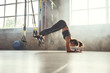 © Friends Stock - Making perfect body. Young athletic woman exercising with suspension straps in the gym