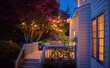 beautifully lit exterior of traditional house with wooden terrace and blooming crape myrtle in summer garden at night