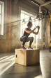 © Friends Stock - Challenging myself. Side view of athletic woman in sportswear doing squat while standing on wooden box at gym