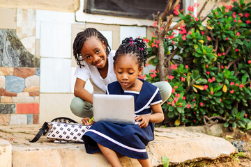 Two young girls sitting on a rock using a laptop