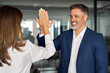 © Stock 4 You - Team of mature Latin business woman and European business man doing high five while discussing project in office. Team of colleagues, partners satisfied with results of team work on project together.