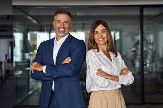 portrait of smiling mature latin or indian business man and european business woman standing arms cr