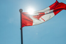 Canadian Flag Blowing In The Wind Against The Sun On A Hot Summer Day