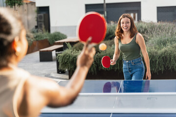 Happy girl friends playing ping pong table tennis, having fun together at the University campus 