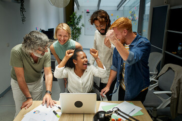 Wall Mural - Group of colleagues at the office raising their arms in celebration a good new. Work success around a laptop. It is a multi-ethnic group. African American woman leads the meeting