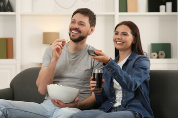 Wall Mural - Happy couple watching show at home. Woman changing TV channels with remote control