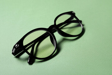 Stylish pair of glasses with black frame on light green background, closeup