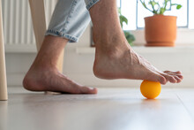 Man Using Ball To Relieve Symptoms Of Arthritis In Foot, Close Up. Person Sitting On Chair At Home Massaging Arthritic Feet To Reduce Pain And Improve Blood Flow, Reflexology And Self-massage Concept