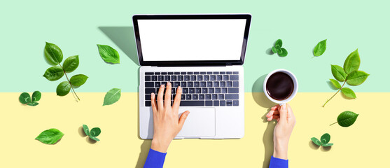 Poster - Person using a laptop computer with green leaves - flat lay