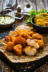 Bakaliaros - seared cod fritters with fried potatoes and fresh vegetables on wooden table 