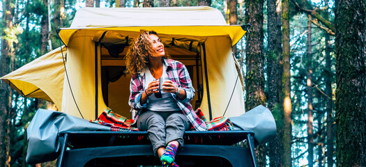 Freedom and alternative camping oslution with roof tent on the car. One adventure woman enjoy alternative vacation alone sitting outside her tent in the forest woods. Freedom and journey lifestyle