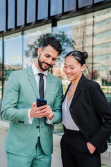 Vertical portrait of a couple of young businesspeople watching their successful stock shares on smartphone. Two partners smiling using a cellphone to invest on market. Coworkers with a mobile phone