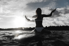 Woman Sitting On Surfboard In Sea Against Sky