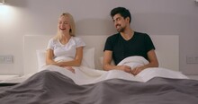 Fair-haired Woman Pretends That She Is Angry And Offended, She Smiling Laughing While Sitting On Bed With Boyfriend, Positive Wife And Husband Have Fun In Bedroom, Positive Emotions